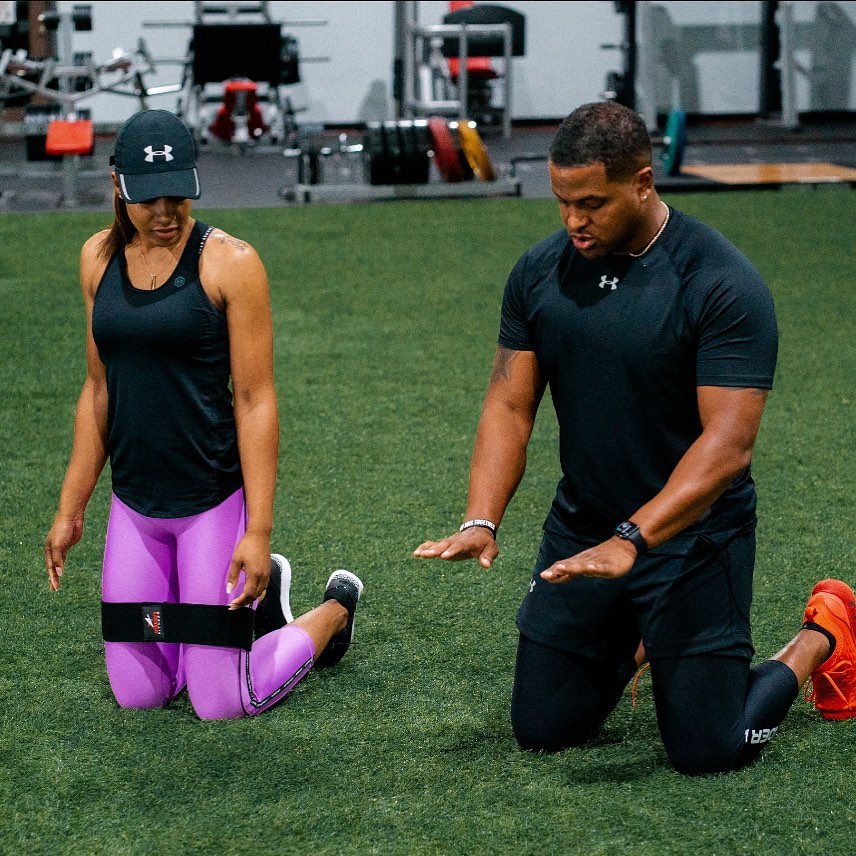 Two people exercising on a grassy field with sports equipment in the background.